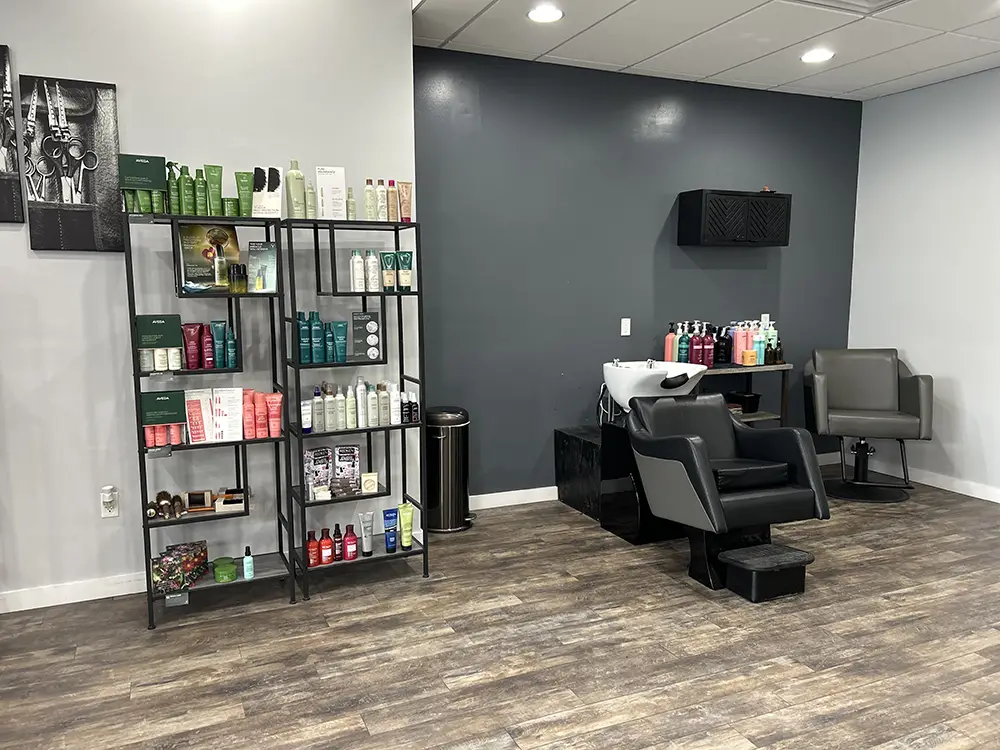 A hair salon interior with a product display shelf on the left and two shampoo stations with chairs and hair care products on the right. - Styles by Stacy - Poughkeepsie, NY
