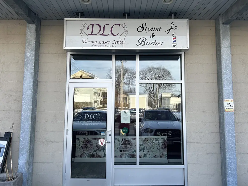 Glass storefront with signs reading "DLC Derma Laser Center" and "Stylist & Barber," reflecting nearby buildings and trees in the windows. - Styles by Stacy - Poughkeepsie, NY